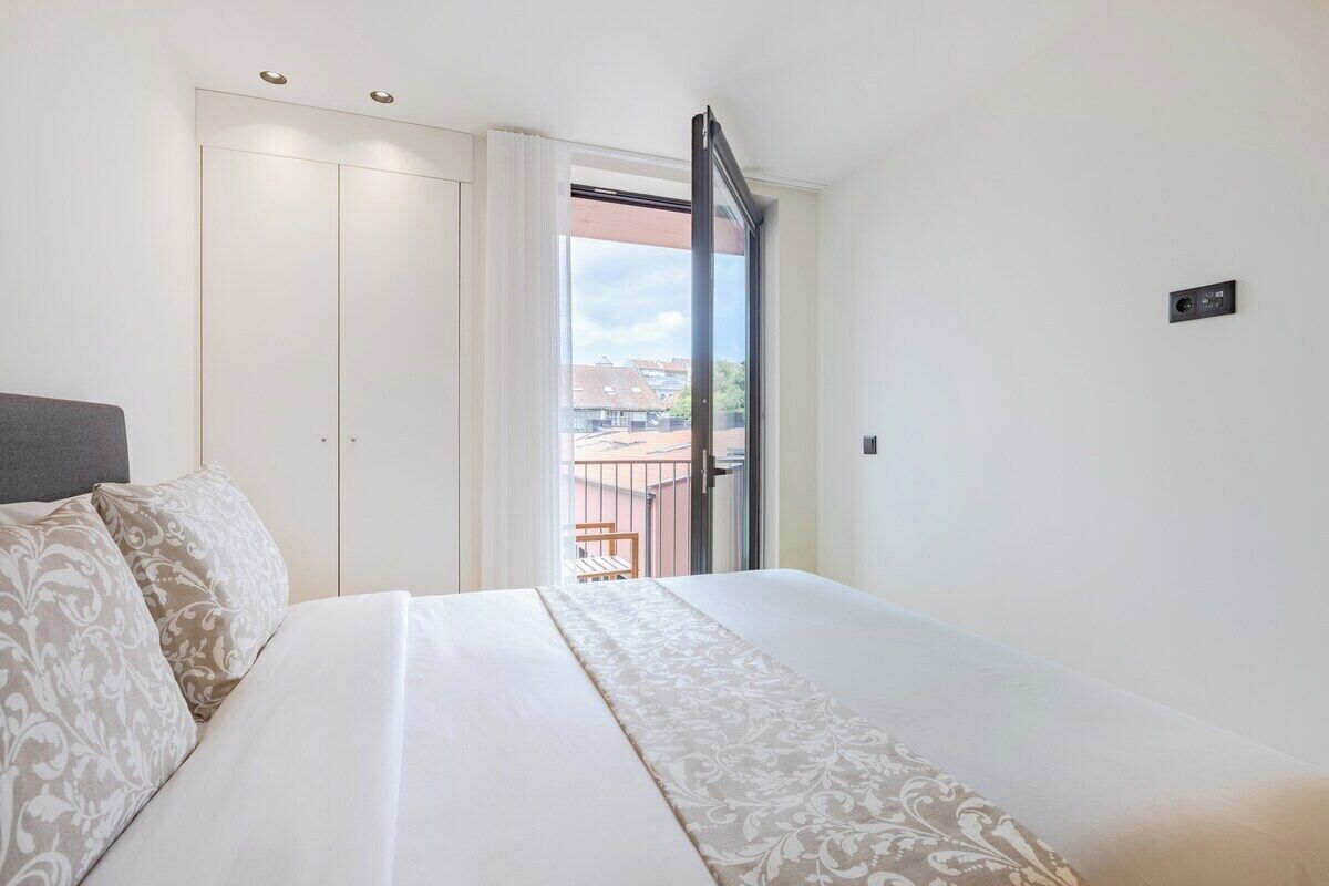 A bedroom with a bed, a wardrobe, a balcony with a view, and a small control panel on the wall.