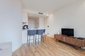 A modern kitchen with two bar stools, a wooden TV stand, and a flat-screen TV. - Balcony Garden Views @ Terracotta Collection (Porto)