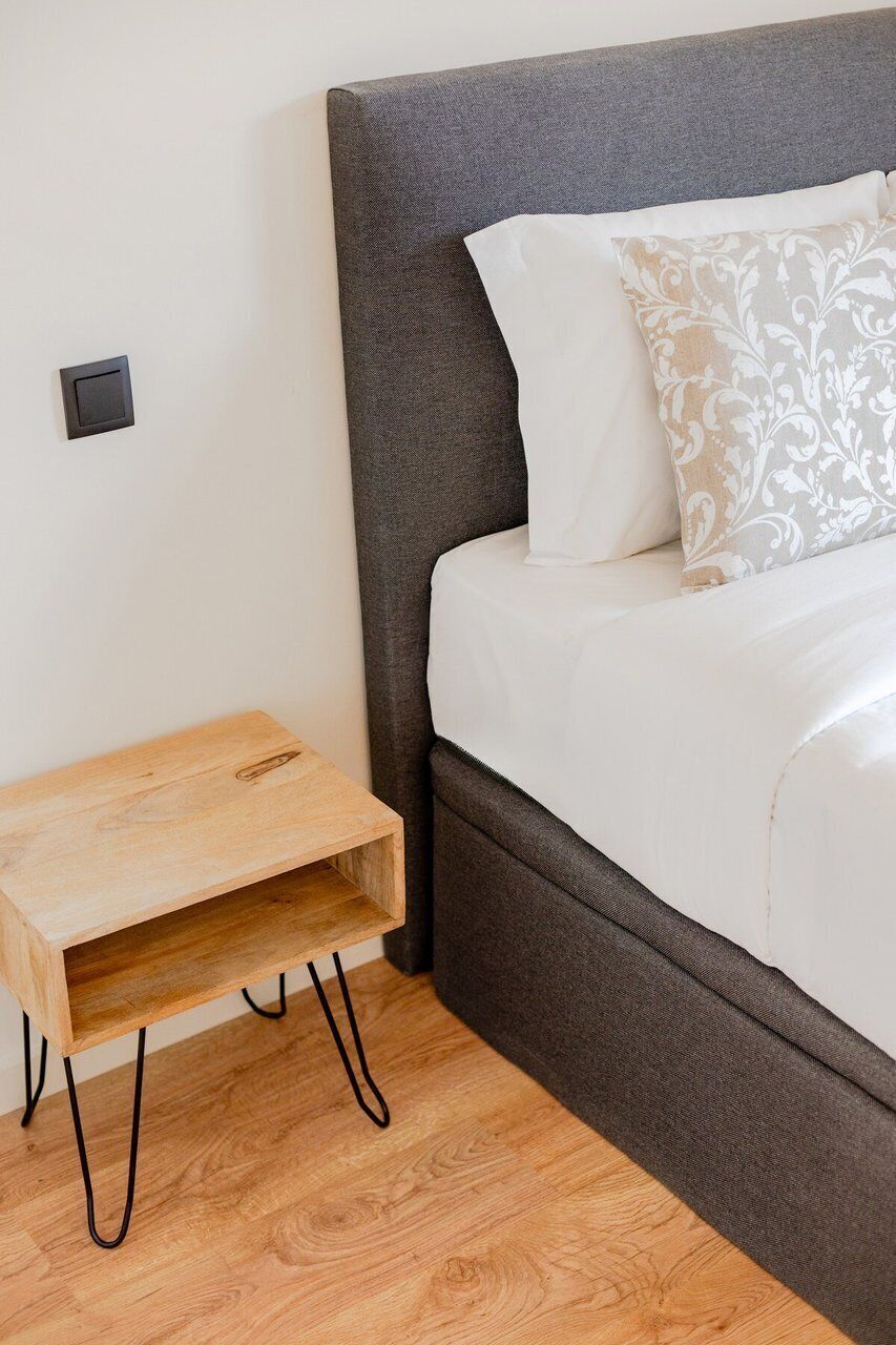 Ein Bett mit grauem Kopfteil, weißer Bettwäsche und einem gemusterten Kopfkissen.