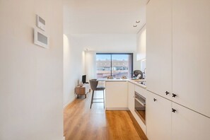 A modern kitchen with a central island, a dining area with a chair, and a view of the city through a window. - Balcony Garden Views @ Terracotta Collection (Porto)