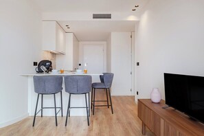 A modern kitchen with a white countertop, three grey bar stools, a wooden cabinet with a TV, and a pink vase. - Balcony Garden Views @ Terracotta Collection (Porto)