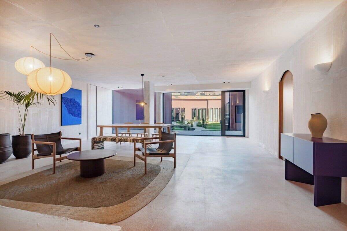 A spacious living area with a round table, chairs, a sofa, and a large window offering a view of the outdoors.