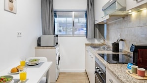 A compact kitchen with a dining area, a window, and a view of the city. - Smart Stay in Gaia | Cozy & Work-Ready (Vila Nova de Gaia)
