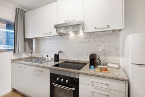 A modern kitchen with white cabinets, a built-in oven, a stovetop, and a window with a view. - Smart Stay in Gaia | Cozy & Work-Ready (Vila Nova de Gaia)
