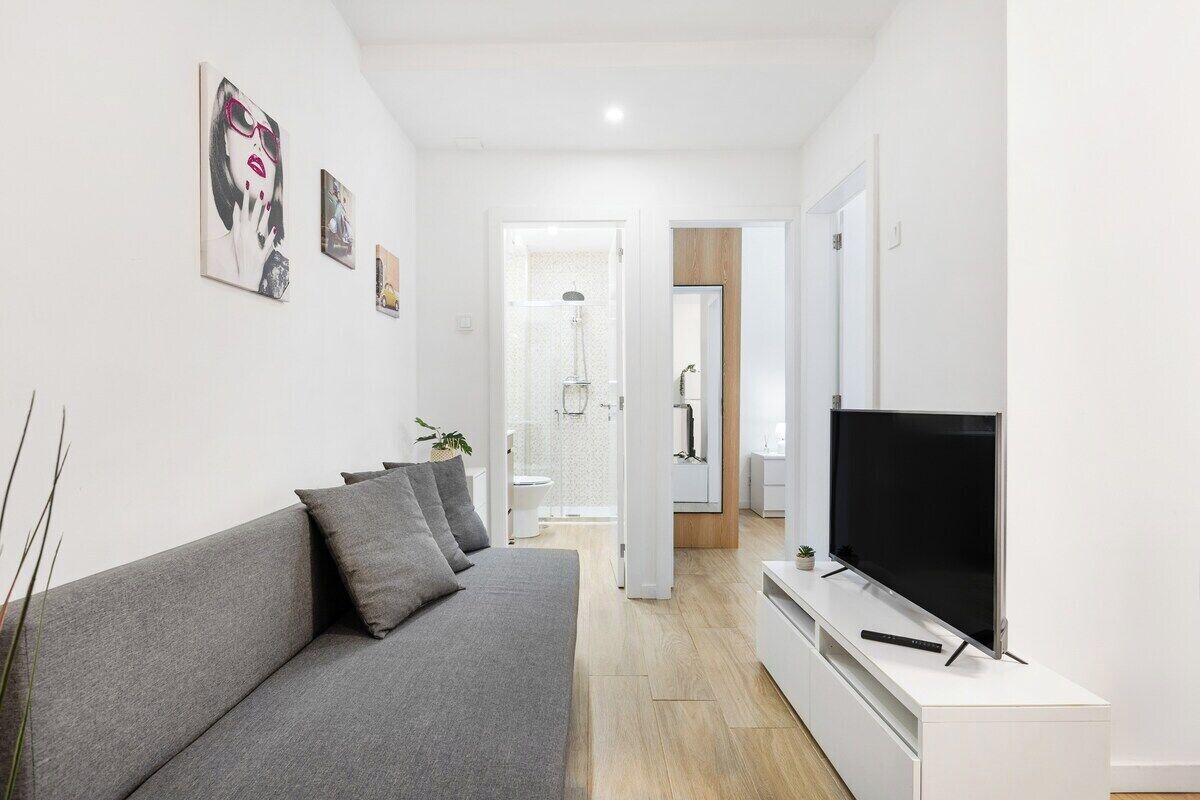 Ein modernes Wohnzimmer mit grauem Sofa, einem Flachbildfernseher und Kunstwerken an den Wänden.