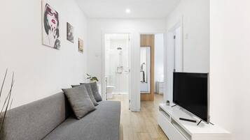 Un salon moderne avec un canapé gris, un téléviseur à écran plat et des œuvres d’art accrochées aux murs.
