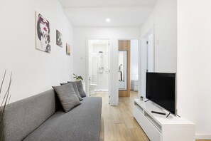 Un salon moderne avec un canapé gris, un téléviseur à écran plat et des œuvres d’art accrochées aux murs.