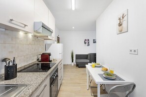 A compact kitchen with a dining area, a microwave, a stove, and a small refrigerator. - Smart Stay in Gaia | Cozy & Work-Ready (Vila Nova de Gaia)