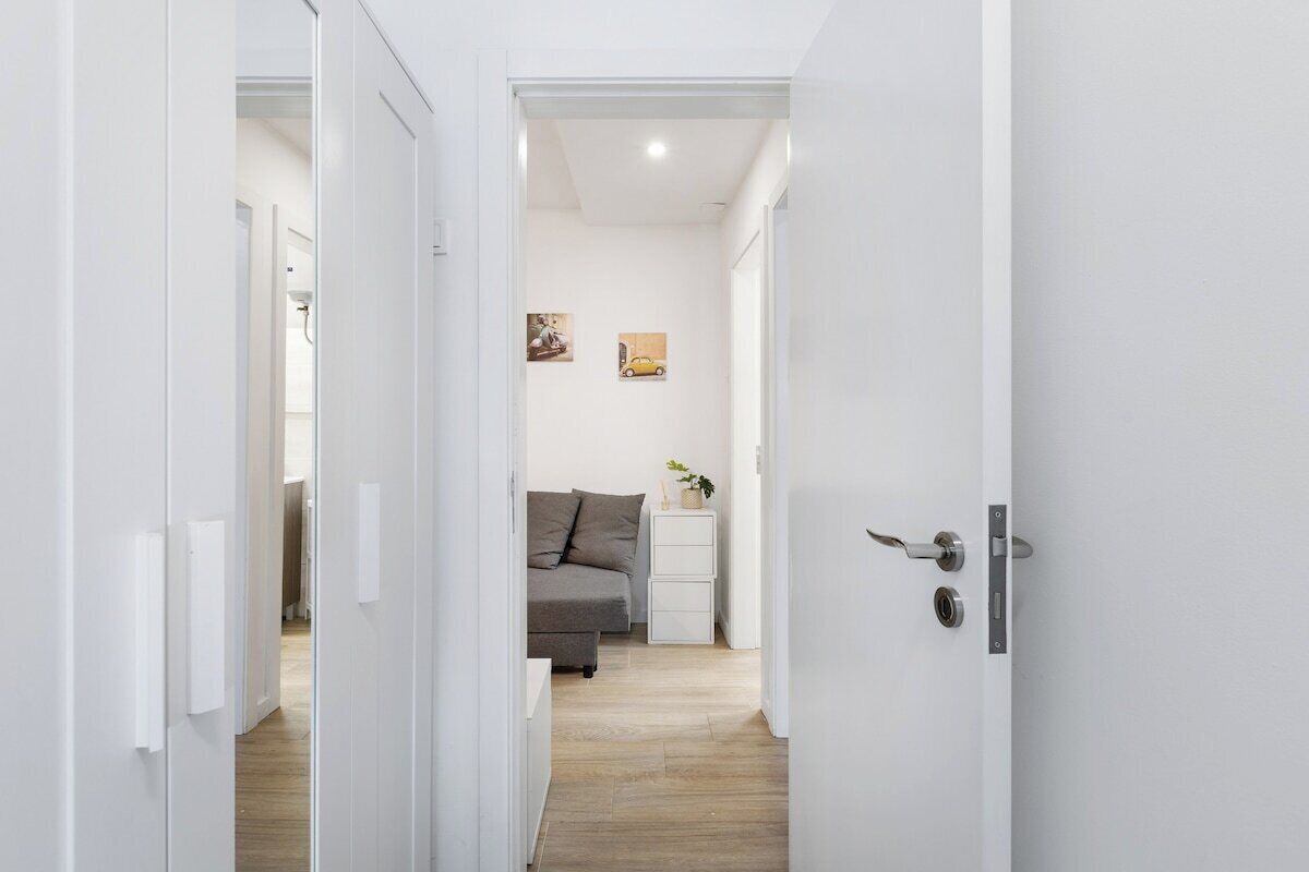 A narrow hallway with a bed, bedside table, and wall art.