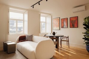 A modern living room with a sofa, a dining table, chairs, and artwork on the wall. - Oasiys - Your Getaway in Porto (Porto)