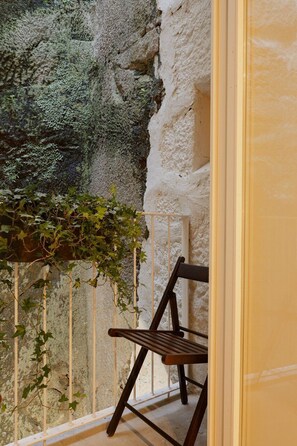 A balcony with a chair, a white railing, and a wall with a textured surface and greenery. - Oasiys - Your Getaway in Porto (Porto)