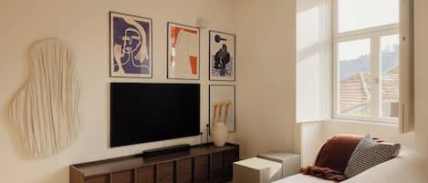 Un dormitorio con una cama, televisión, ventana y obras de arte en la pared.