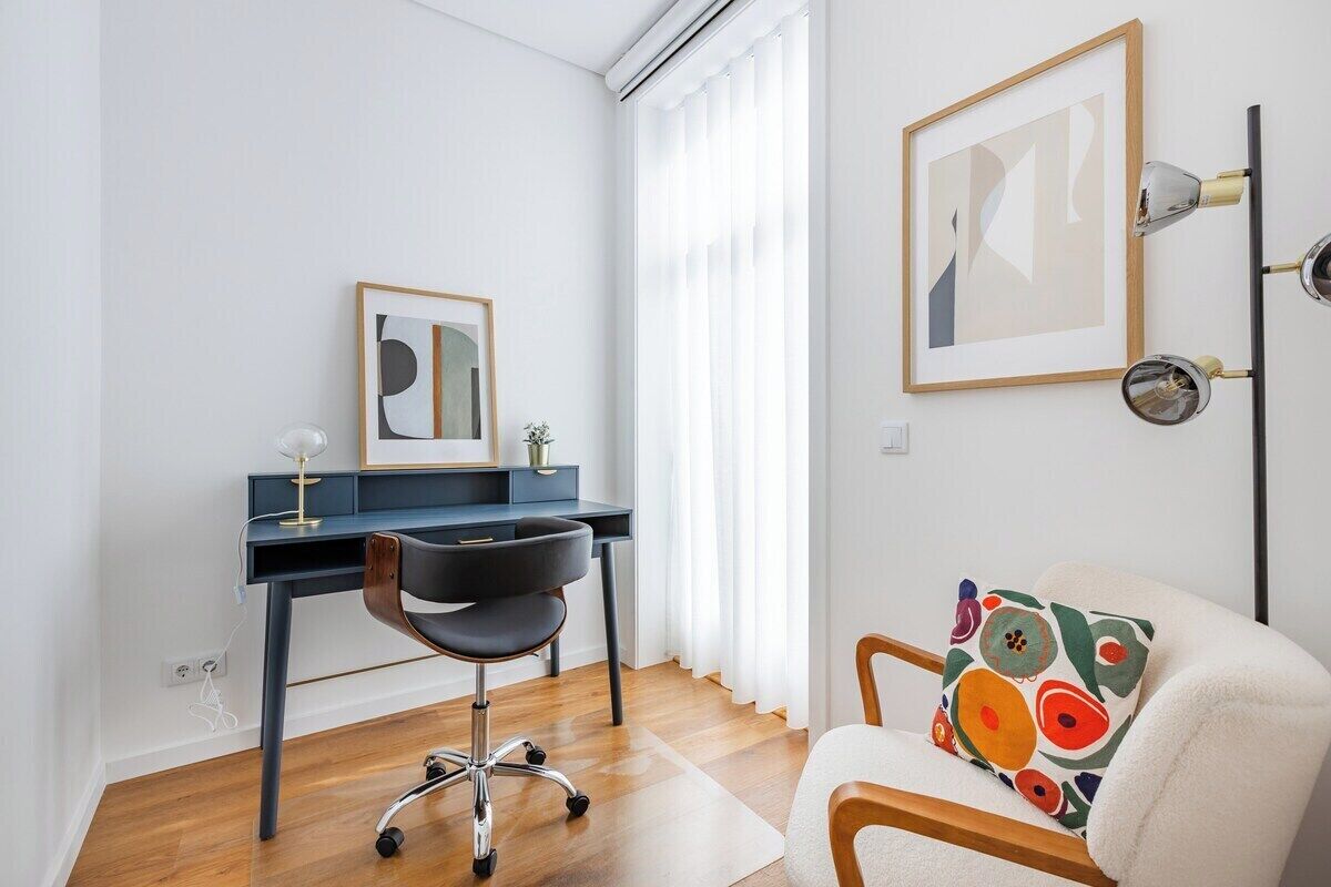Una habitación moderna con escritorio, silla y sofá con un cojín colorido.