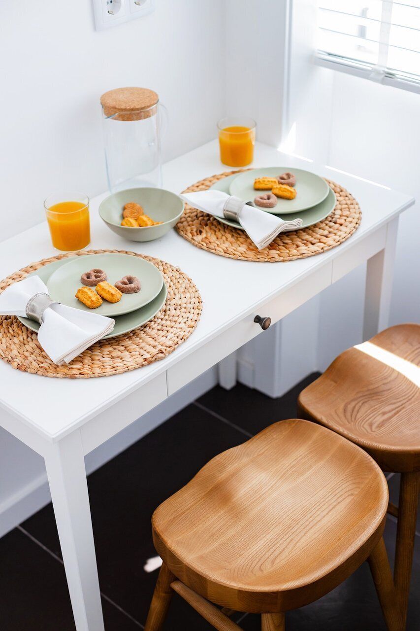 Una mesa de comedor blanca con dos platos de comida, un vaso de zumo de naranja y un tarro.