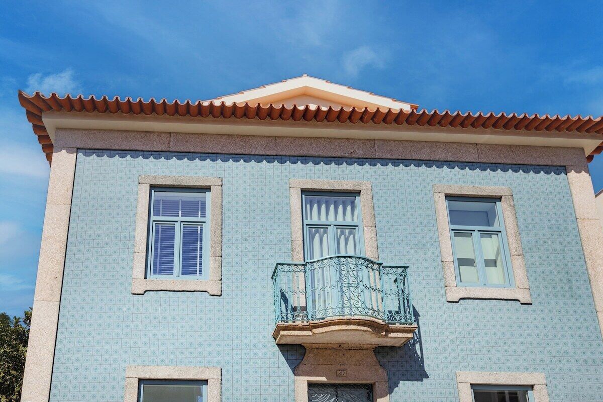 Un edificio con fachada de azulejos, un balcón con barandilla de metal decorativa y un tejado a dos aguas.