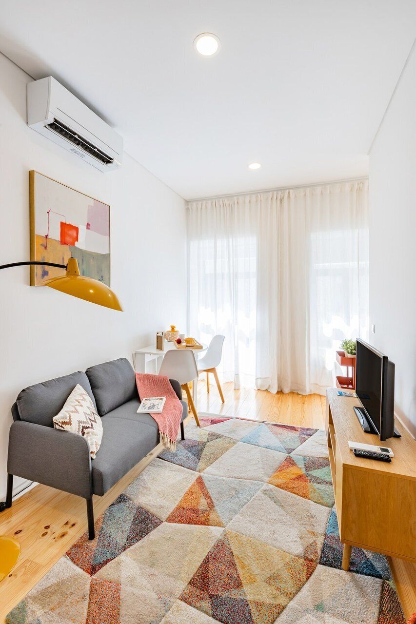 A modern living room with a sofa, a coffee table, a TV, and a patterned rug.