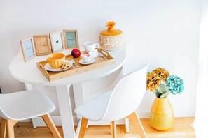 Ein weißer Tisch mit Tablett, gerahmte Bilder, ein gelber Blumenstrauß und weiße Stühle.