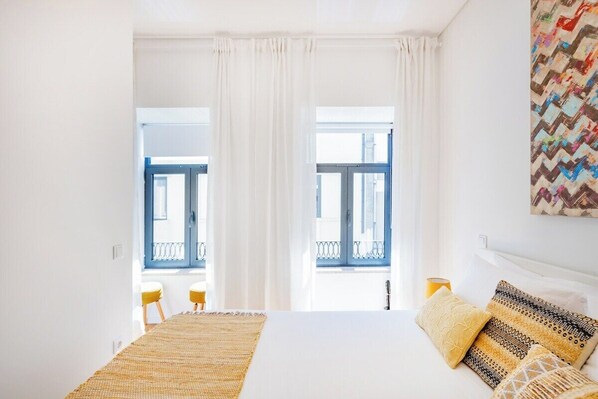 Ein Hotelzimmer mit Bett, einem Vorhangfenster, Blick auf einen Außenbalkon und einem Bild an der Wand.