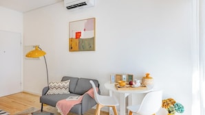 Uma sala de estar moderna com sofá, mesa de jantar com cadeiras, abajur e ar condicionado fixado na parede.