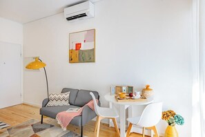 Ein modernes Wohnzimmer mit einer Couch, einem Esstisch mit Stühlen, einer Stehlampe und einer Wand-Klimaanlage.