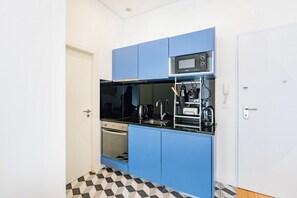 A compact kitchen with blue cabinets, a black countertop, a microwave, and a kettle. - Oporto Urban Mood with AC | Bonfim Studio (Porto)