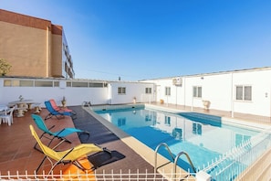 Ein Pool auf dem Dach mit Liegestühlen, einem Tisch und einem Gebäude im Hintergrund.