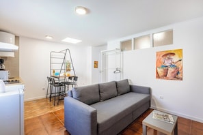 Ein modernes Wohnzimmer mit grauem Sofa, einem Esstisch mit Stühlen, einer Strickleiter und einer Küchenzeile mit Herd.