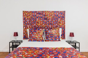 Ein Bett mit einer farbenfrohen Steude, ein Kopfteil mit Muster und zwei Nachttische mit Lampen.