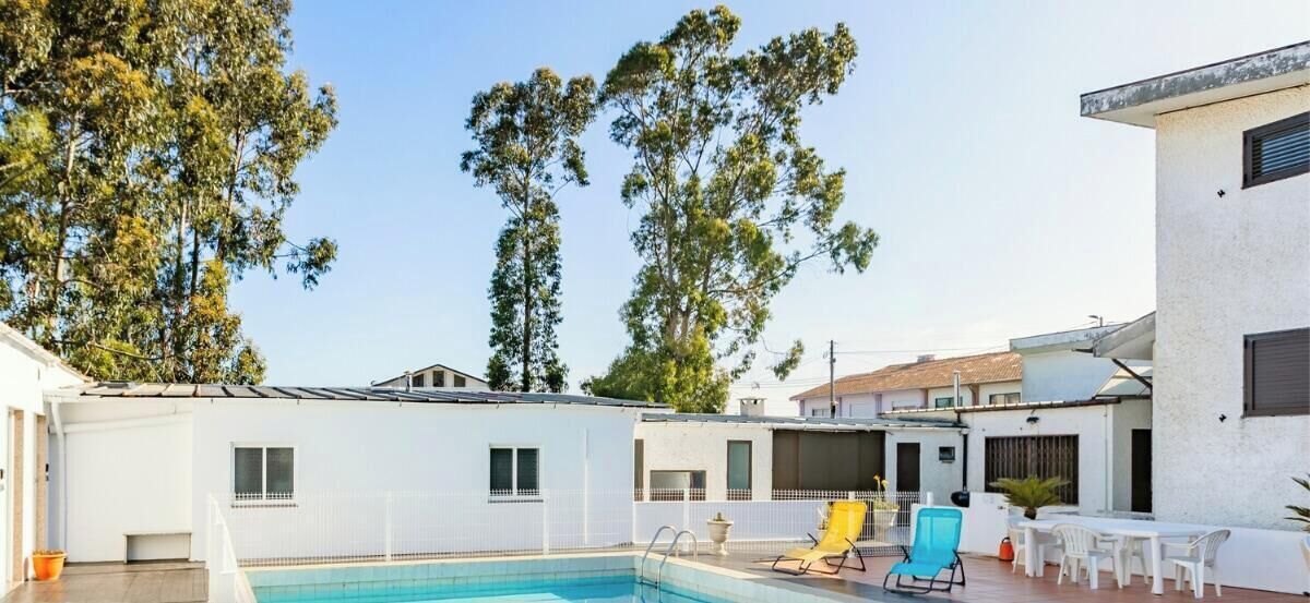 A pool area with a clear sky, trees, and a building with a white exterior.