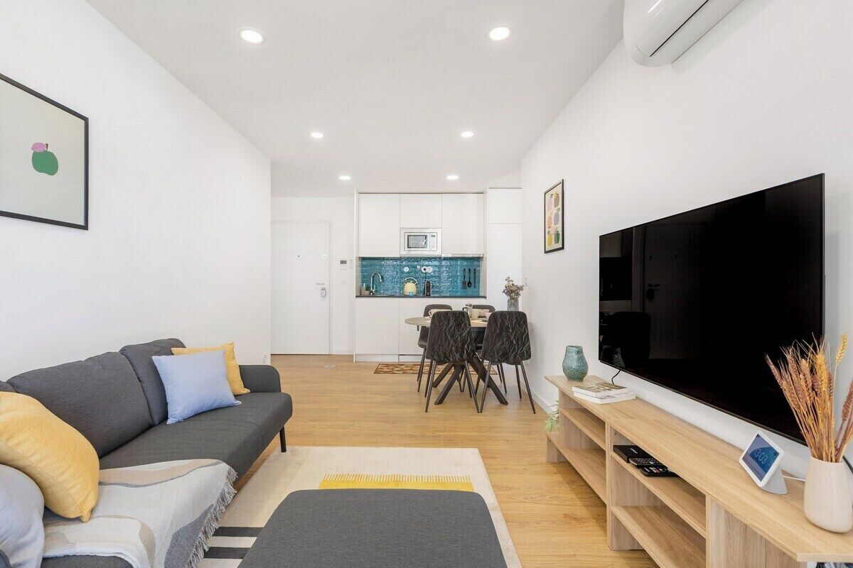A modern living room with a sofa, TV, and a dining area with chairs and a table.
