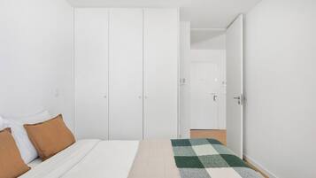 Une chambre à coucher avec un lit, deux oreillers marron, une couverture à carreaux, une armoire et une porte donnant sur une autre pièce.