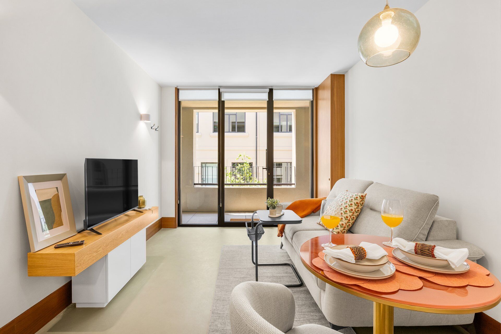 A modern living room with a TV, sofa, dining table, and a balcony with a view.