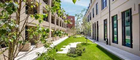 A courtyard with modern buildings, a well-maintained lawn, and a clear sky.