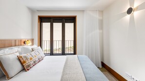 Ein Hotelzimmer mit Bett, Nachttisch, Lampe, Fenster mit Blick und einer Wandleuchte.