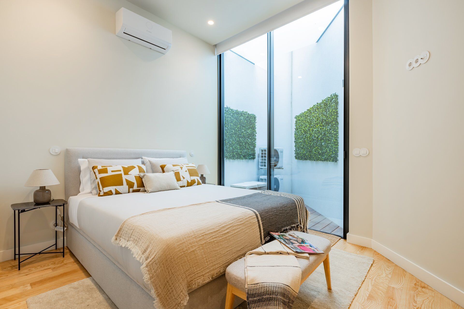 Une chambre moderne avec un lit, une table de chevet, une lampe et une vue sur la verdure grâce à une porte vitrée.
