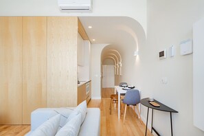 A modern living room with a sofa, a dining area with a table and chairs, and a kitchen in the background. - Modern 1BR with AC | Casa da Música (Porto)