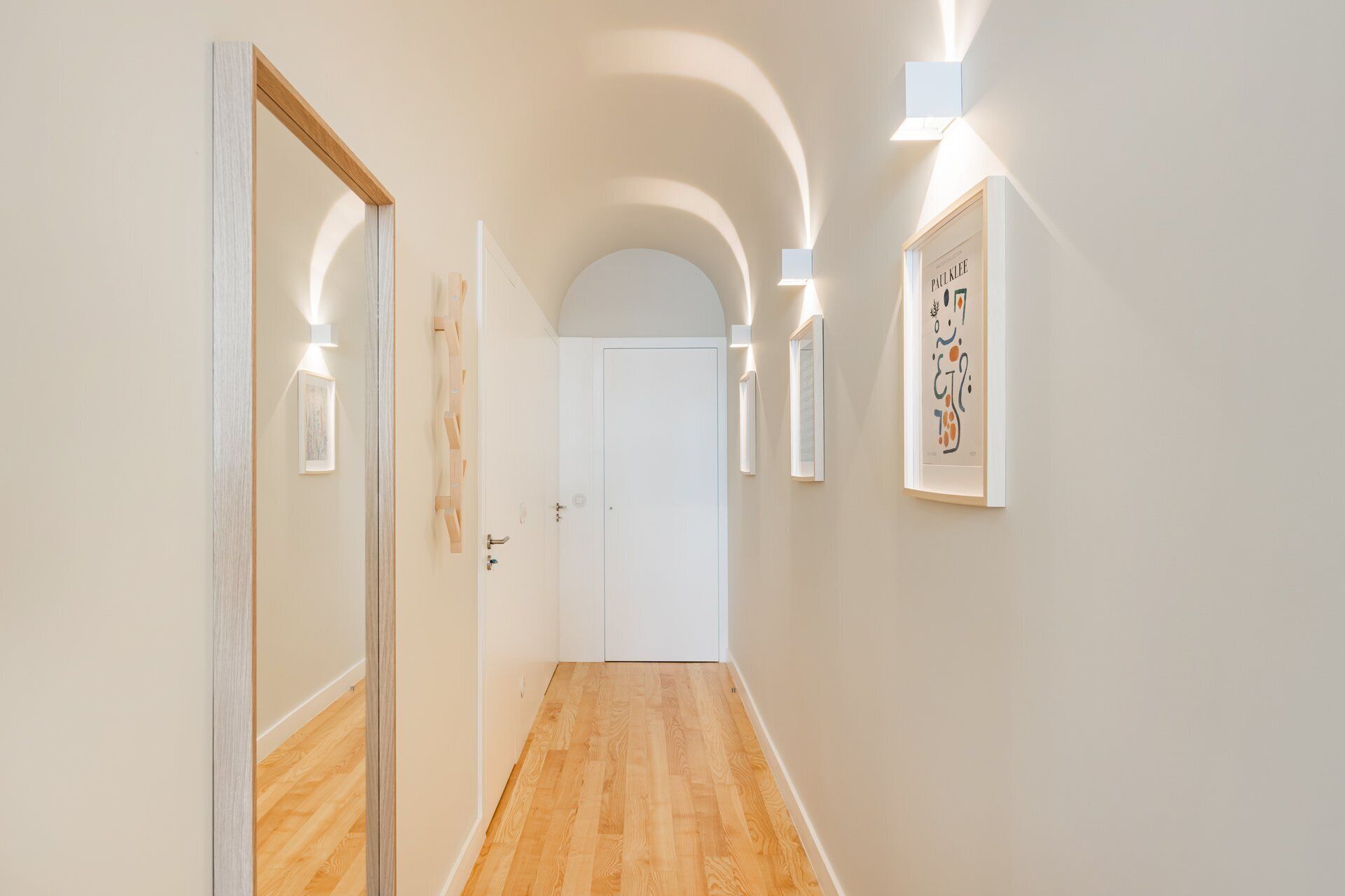 Un couloir doté d’un plancher en bois, de murs blancs et d’une porte blanche au fond.