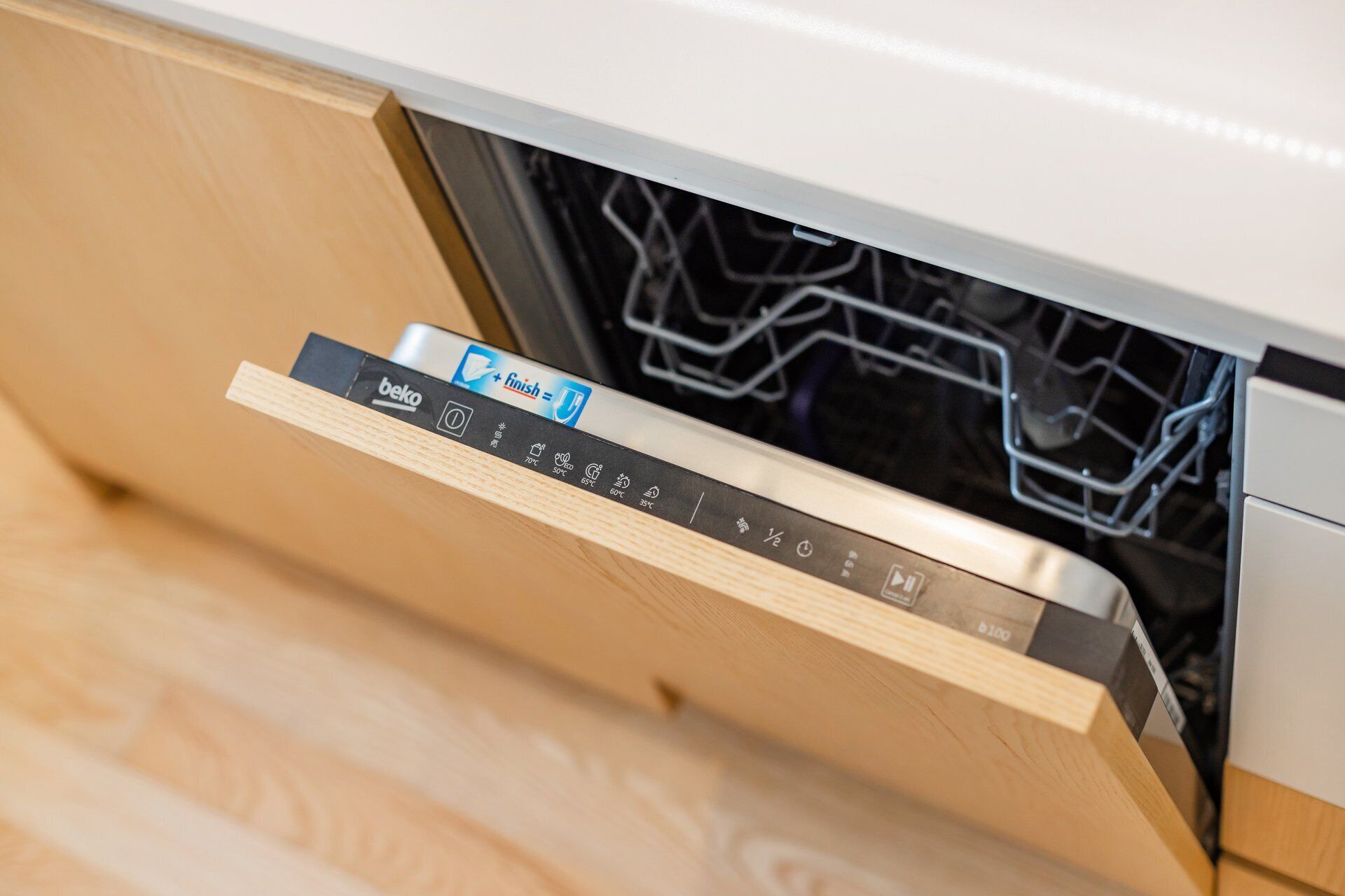 A dishwasher drawer with a control panel displaying temperature settings and a detergent package.