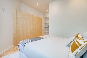 A bedroom with a bed, a wooden wardrobe, a white shelf unit, and a white carpet. - Modern 1BR with AC | Casa da Música (Porto)