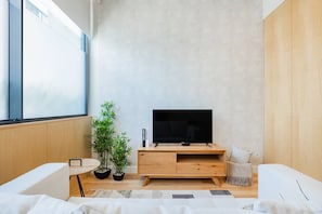 Ein modernes Wohnzimmer mit Fernseher, Holzmöbeln, einer Topfpflanze und einem großen Fenster.