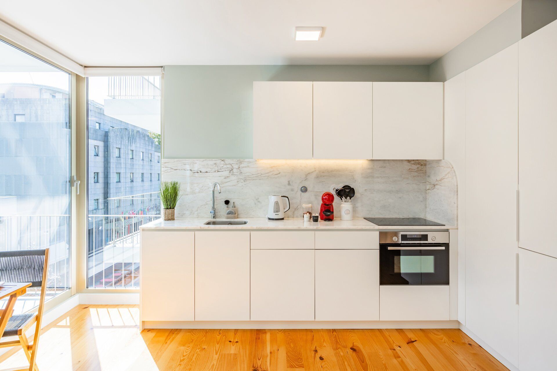 A modern kitchen with white cabinetry, a marble backsplash, and a wooden floor.