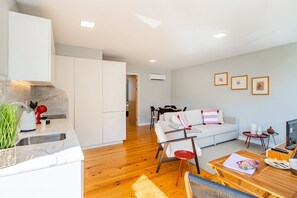 A modern living space with a kitchen, dining area, and a sofa. - Bright Boavista Flat | Balcony & AC (Porto)