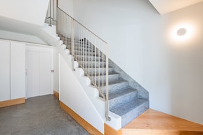 A staircase with a metal railing, carpeted steps, and a wooden floor. - Bright Boavista Flat | Balcony & AC (Porto)