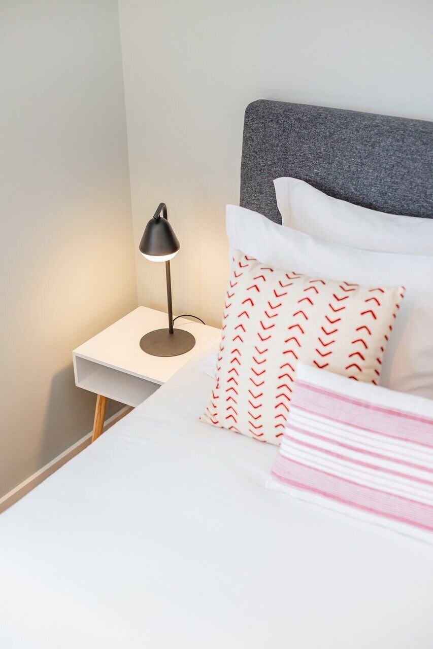 A neatly made bed with pillows and a bedside lamp on a white nightstand.