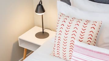 A neatly made bed with pillows and a bedside lamp on a white nightstand.