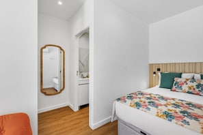 A bedroom with a wooden headboard, a bed with floral bedding, a mirror, and a bathroom with a marble wall. - Porto Garden | Private Patio Studio (Porto)
