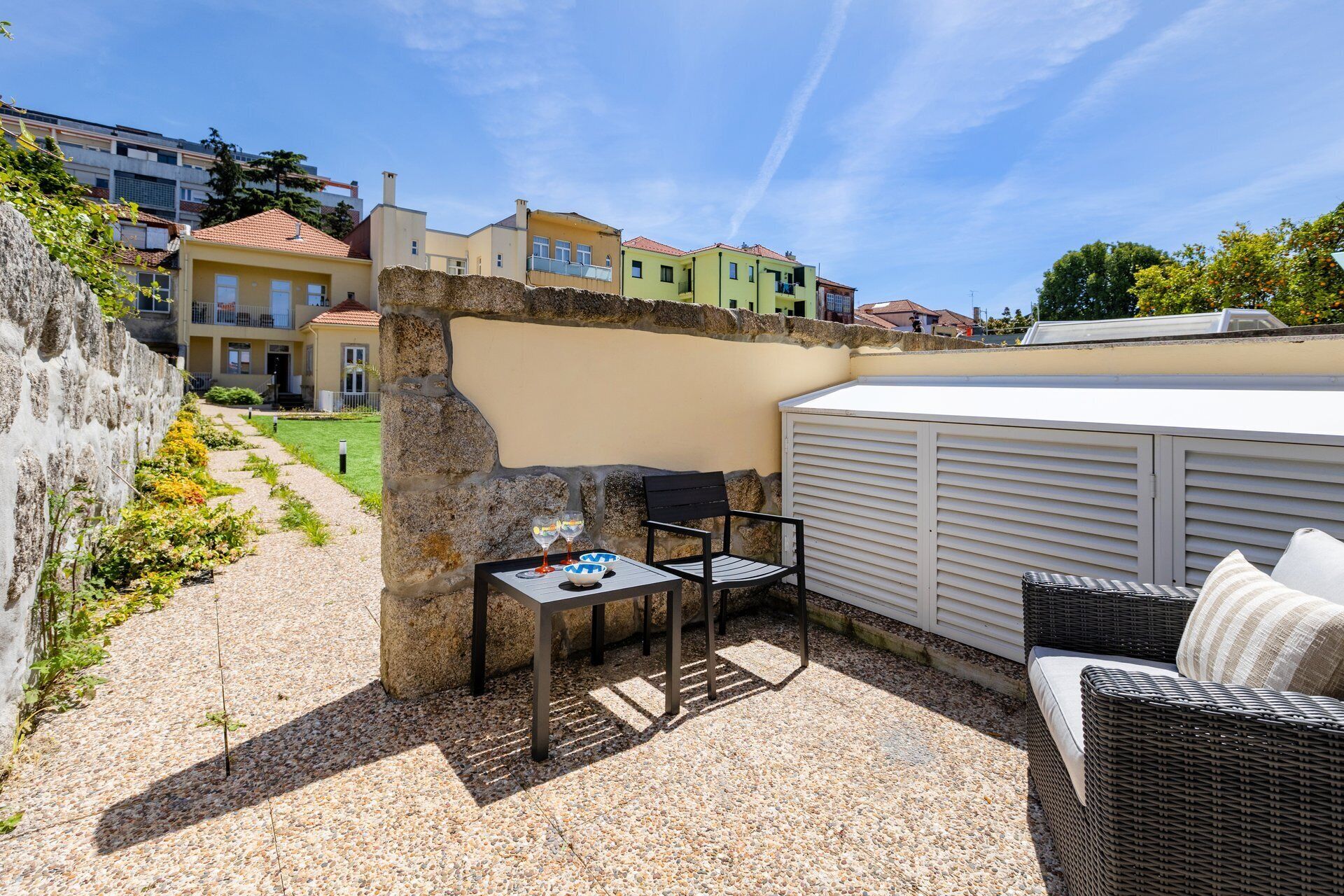 Eine Terrasse mit einer Steinmauer, einem Tisch mit zwei Stühlen und einer Korbschaukel.