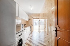 A kitchen with a washing machine, a microwave, and a tiled floor. - Ildefonso Oporto Stay (Porto)