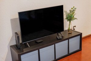 Een flatscreen televisie op een donker houten dressoir, met een bloemenvaas en een afstandsbediening.