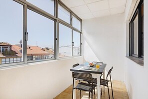 A balcony with a table and chairs, a window with a view of buildings, and a tiled floor. - Ildefonso Oporto Stay (Porto)